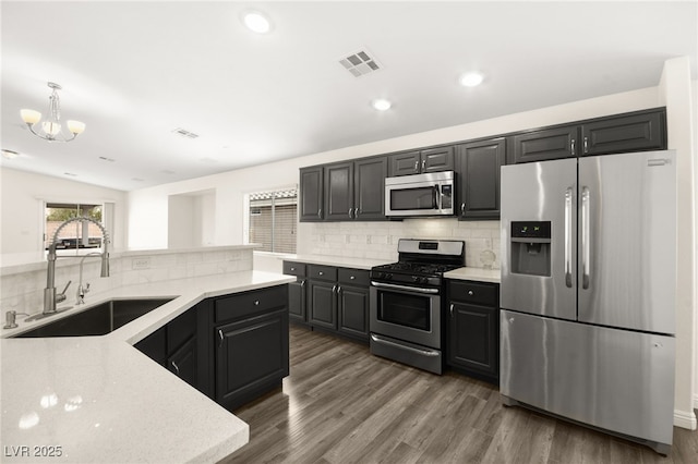 kitchen featuring appliances with stainless steel finishes, tasteful backsplash, sink, hanging light fixtures, and dark wood-type flooring