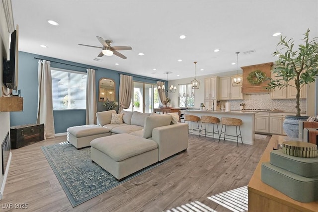 living room with ceiling fan with notable chandelier and light wood-type flooring