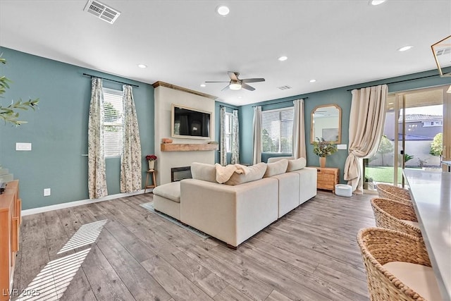 living room with ceiling fan, light wood-type flooring, and a fireplace