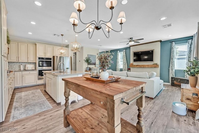 kitchen with pendant lighting, appliances with stainless steel finishes, a kitchen island with sink, and cream cabinetry