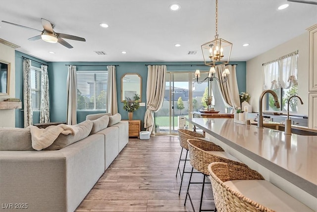 living room featuring ceiling fan with notable chandelier, plenty of natural light, sink, and light wood-type flooring