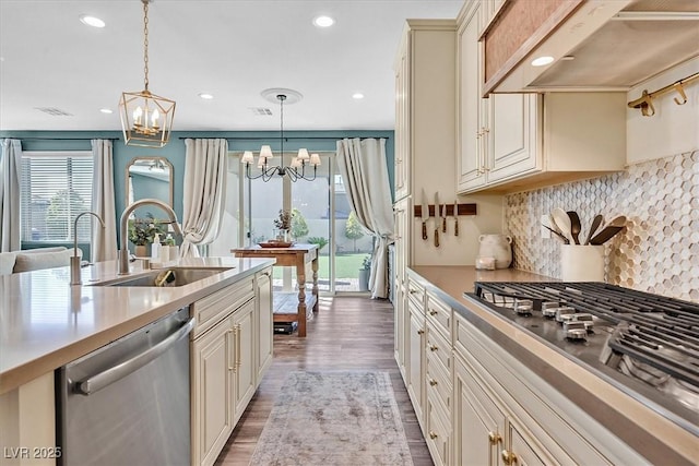 kitchen with pendant lighting, sink, appliances with stainless steel finishes, cream cabinets, and custom exhaust hood