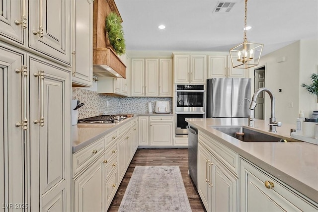 kitchen with sink, appliances with stainless steel finishes, tasteful backsplash, decorative light fixtures, and cream cabinetry