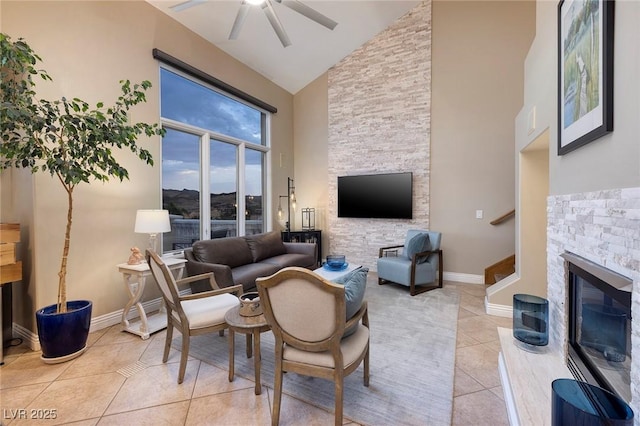 tiled living room featuring ceiling fan, a stone fireplace, and high vaulted ceiling