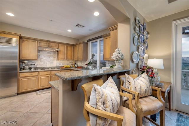 kitchen with appliances with stainless steel finishes, dark stone countertops, light tile patterned floors, and kitchen peninsula