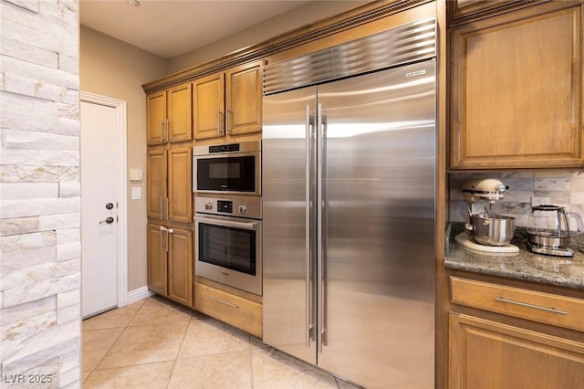 kitchen featuring dark stone countertops, light tile patterned floors, backsplash, and built in refrigerator