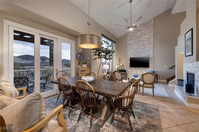 tiled dining area featuring ceiling fan, a stone fireplace, a mountain view, and high vaulted ceiling