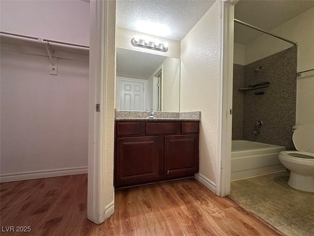 full bathroom with tiled shower / bath, hardwood / wood-style flooring, vanity, toilet, and a textured ceiling