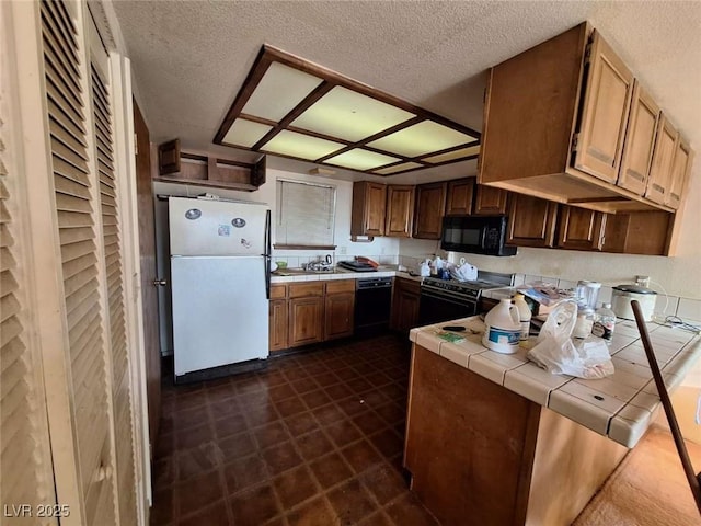 kitchen with tile counters, black appliances, and a textured ceiling