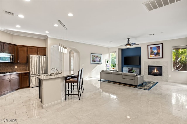 kitchen featuring appliances with stainless steel finishes, a breakfast bar, ceiling fan, light stone countertops, and a center island with sink