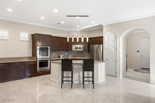 kitchen featuring light stone counters, dark brown cabinets, appliances with stainless steel finishes, a kitchen breakfast bar, and a kitchen island with sink