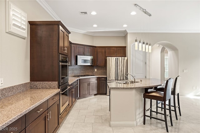 kitchen featuring sink, light stone counters, dark brown cabinets, stainless steel appliances, and a kitchen island with sink