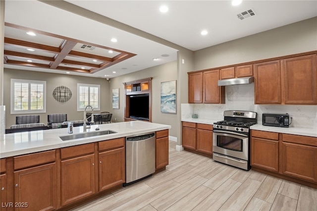 kitchen with coffered ceiling, sink, light wood-type flooring, stainless steel appliances, and decorative backsplash