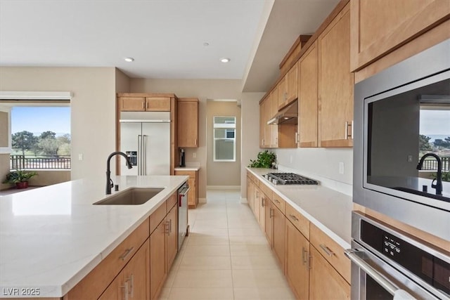 kitchen with sink, appliances with stainless steel finishes, an island with sink, light tile patterned flooring, and light brown cabinetry