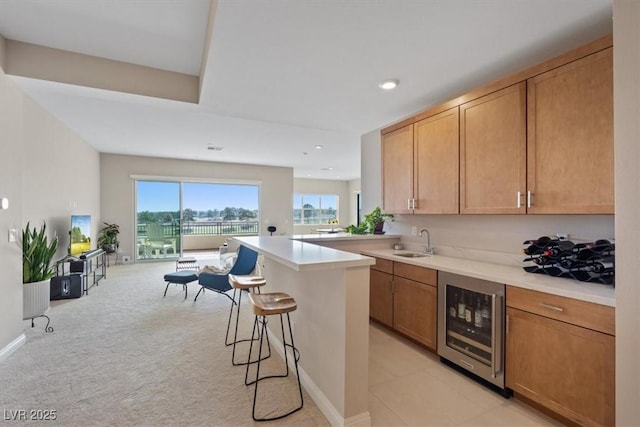 kitchen with a kitchen bar, sink, a center island, light carpet, and beverage cooler