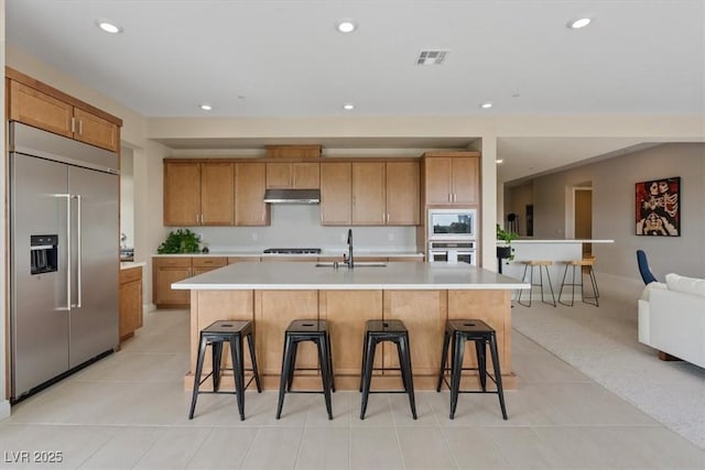 kitchen featuring a kitchen bar, built in appliances, sink, and a large island with sink