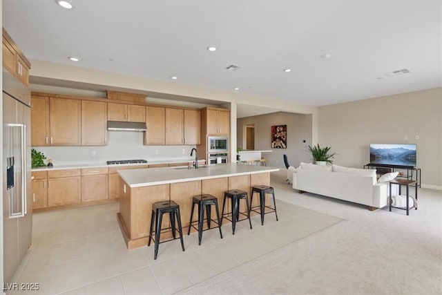 kitchen featuring built in appliances, sink, an island with sink, and light brown cabinets