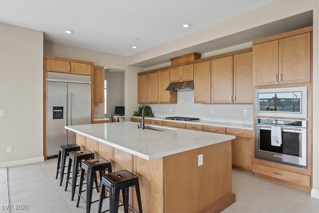 kitchen with sink, light stone counters, built in appliances, light tile patterned floors, and an island with sink