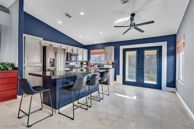 kitchen with vaulted ceiling, appliances with stainless steel finishes, a kitchen bar, a center island, and french doors