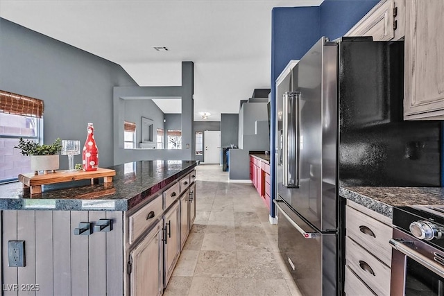 kitchen with plenty of natural light, vaulted ceiling, dark stone counters, and light brown cabinets