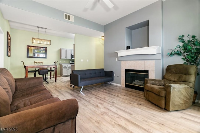 living room featuring ceiling fan, a fireplace, and light hardwood / wood-style floors