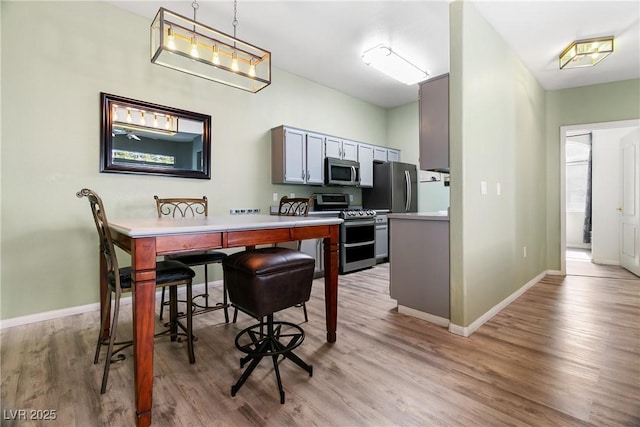 kitchen with gray cabinetry, decorative light fixtures, light hardwood / wood-style floors, and appliances with stainless steel finishes