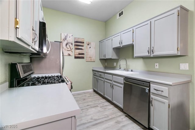 kitchen with stainless steel appliances, gray cabinets, sink, and light hardwood / wood-style flooring