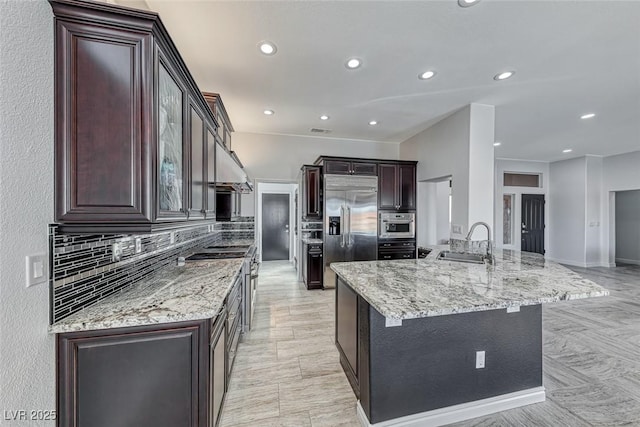 kitchen featuring high end appliances, tasteful backsplash, a sink, dark brown cabinets, and light stone countertops