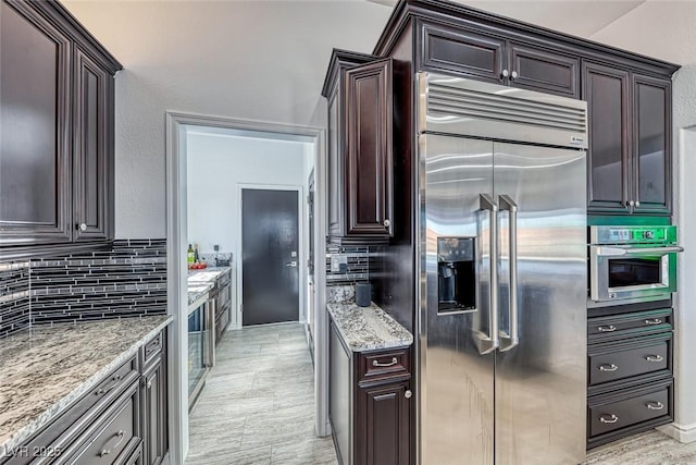 kitchen featuring tasteful backsplash, light stone counters, stainless steel appliances, and dark brown cabinets