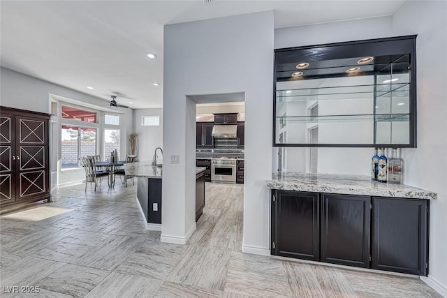 bar featuring oven, recessed lighting, under cabinet range hood, baseboards, and backsplash