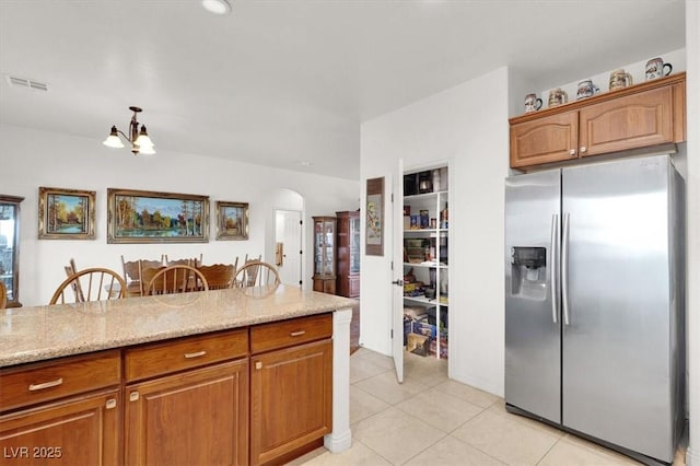 kitchen with decorative light fixtures, light tile patterned floors, a notable chandelier, light stone counters, and stainless steel refrigerator with ice dispenser