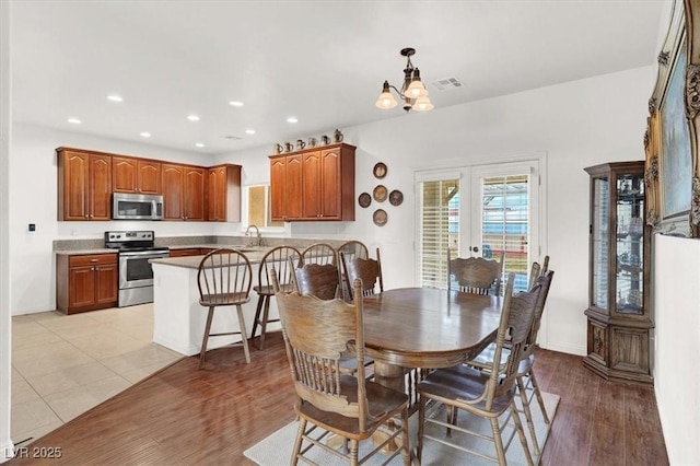 dining space featuring french doors, a notable chandelier, sink, and light wood-type flooring