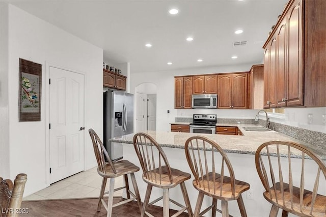 kitchen with light tile patterned flooring, a breakfast bar, sink, light stone counters, and stainless steel appliances