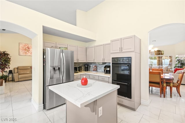 kitchen featuring stainless steel fridge, gray cabinets, a kitchen island, black double oven, and decorative backsplash