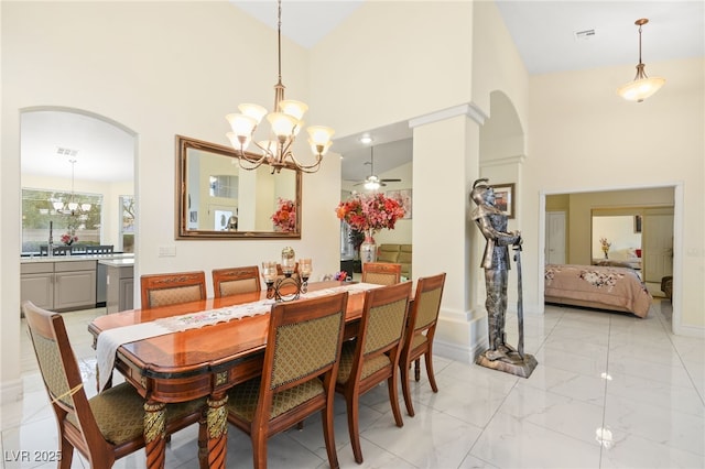 dining area with a towering ceiling and ceiling fan with notable chandelier