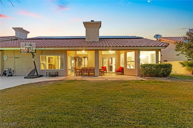 back house at dusk with a patio, a lawn, and solar panels