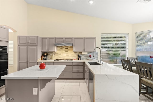 kitchen featuring gray cabinets, sink, backsplash, a center island, and light stone countertops