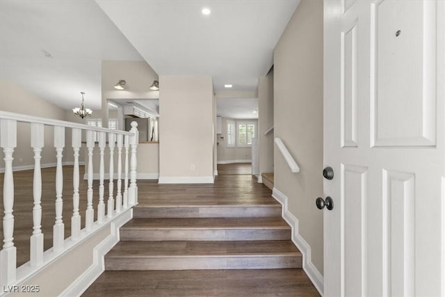 staircase with an inviting chandelier, baseboards, and wood finished floors