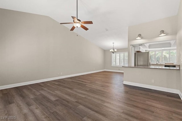 unfurnished living room featuring ceiling fan with notable chandelier, vaulted ceiling, dark wood finished floors, and baseboards