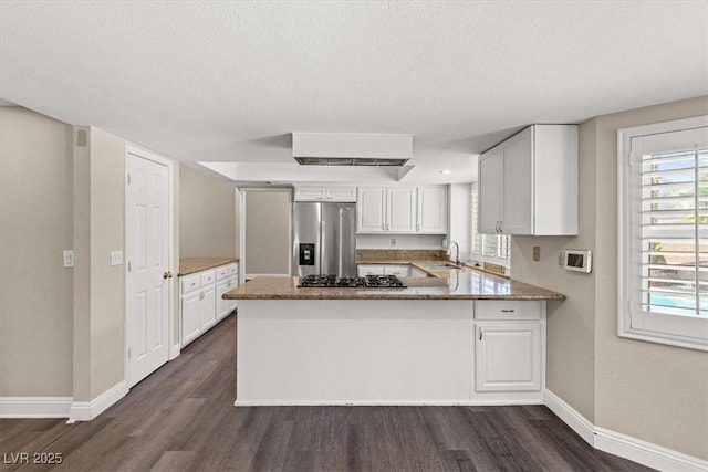 kitchen with appliances with stainless steel finishes, white cabinets, dark wood finished floors, and a peninsula