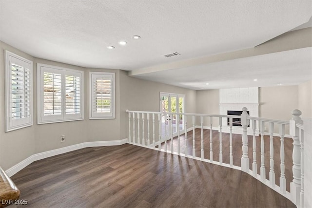 empty room featuring a textured ceiling, recessed lighting, a fireplace, wood finished floors, and baseboards