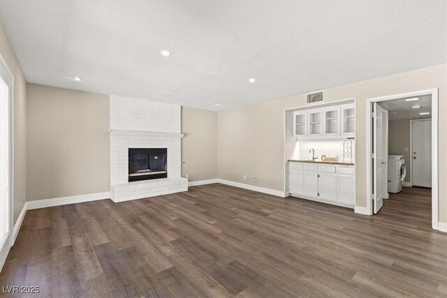 unfurnished living room with a fireplace, dark hardwood / wood-style floors, washer and clothes dryer, and sink