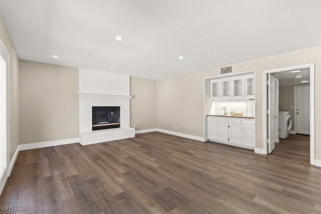 unfurnished living room featuring a fireplace, dark wood finished floors, visible vents, a sink, and separate washer and dryer