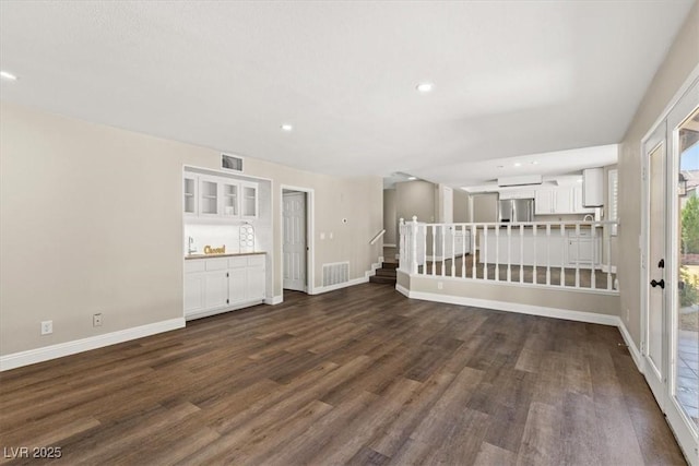 empty room with dark wood-style flooring, visible vents, stairway, and baseboards