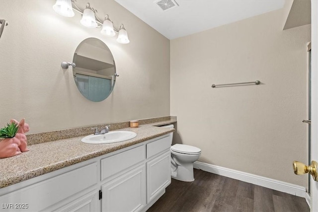 bathroom with visible vents, toilet, vanity, wood finished floors, and baseboards