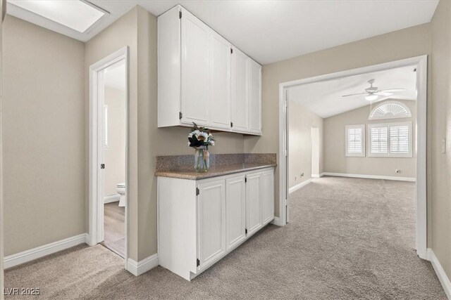 kitchen featuring light carpet, ceiling fan, lofted ceiling with skylight, and white cabinets