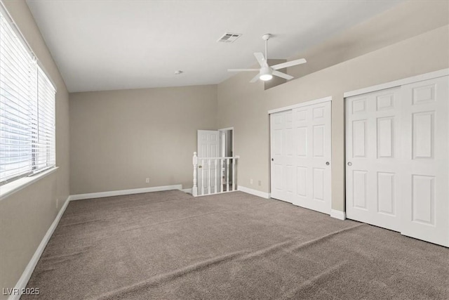 unfurnished bedroom featuring baseboards, visible vents, vaulted ceiling, carpet floors, and two closets