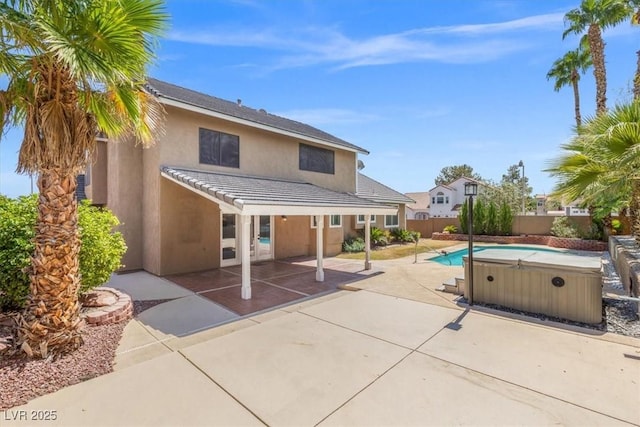 rear view of house featuring a hot tub, a patio, a tile roof, fence, and stucco siding