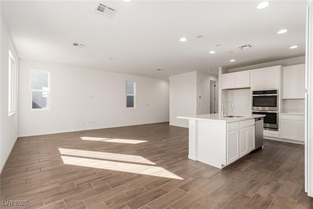 kitchen featuring white cabinetry, sink, a center island with sink, and stainless steel double oven