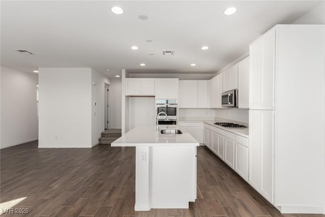 kitchen with dark wood-type flooring, sink, white cabinetry, appliances with stainless steel finishes, and a kitchen island with sink